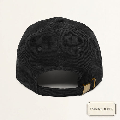 Angled view of a black corduroy dad cap with off-white embroidered DADDY text