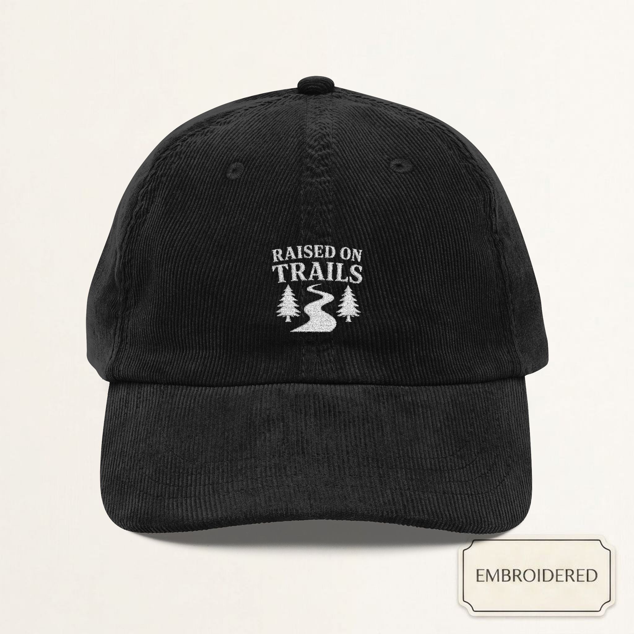 Black corduroy dad cap with small off-white embroidered RAISED ON TRAILS text on the front panel