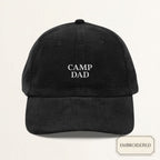 Black corduroy dad cap with small off-white embroidered CAMP DAD text on the front panel