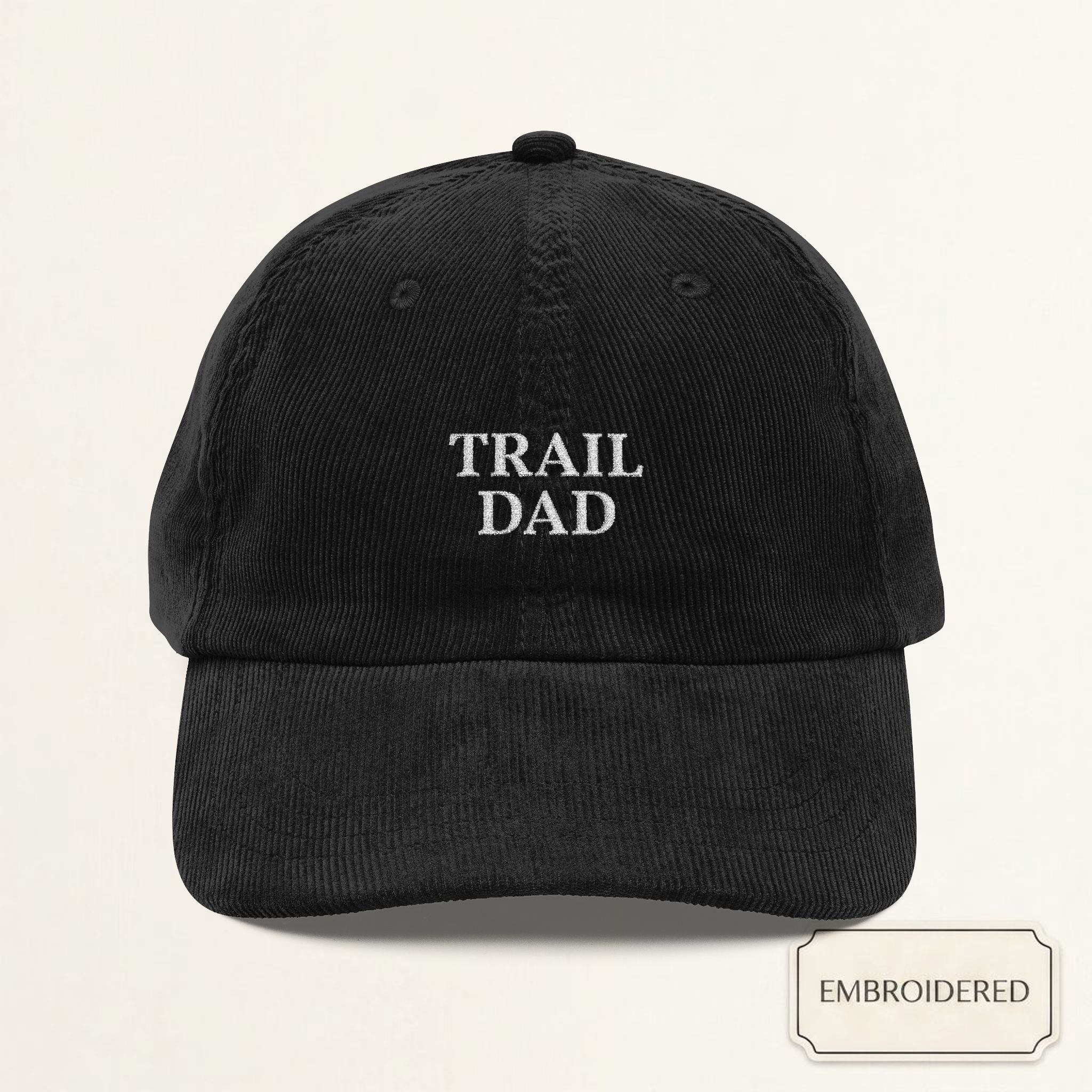 Black corduroy dad cap with small off-white embroidered TRAIL DAD text on the front panel